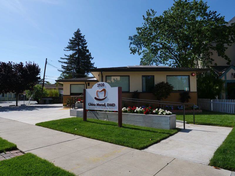 The image shows a single-story house with a sign in front that reads 1900 CHILDREN S HOSPITAL. There is a lawn and a sidewalk, and the sky is clear.