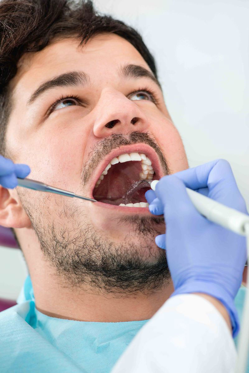 A man in a dental chair receiving a dental treatment with a dentist using specialized tools.