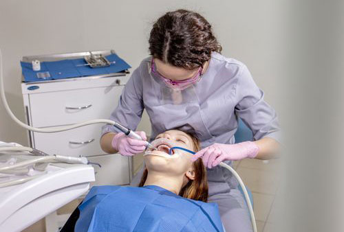 A dental hygienist is performing a teeth cleaning procedure on a patient using an electric toothbrush and dental tools.