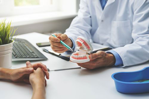 A dentist is examining a patient s teeth, with the patient seated and holding a toothbrush. The setting appears to be a dental office.