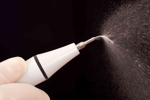 The image shows a close-up of an electric toothbrush with a visible brush head and a stream of water or solution being sprayed from it.