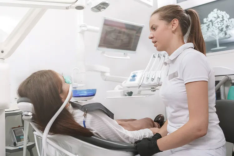 A dental professional in a white lab coat attends to a patient in a dental chair, with both individuals focused on the dental equipment.